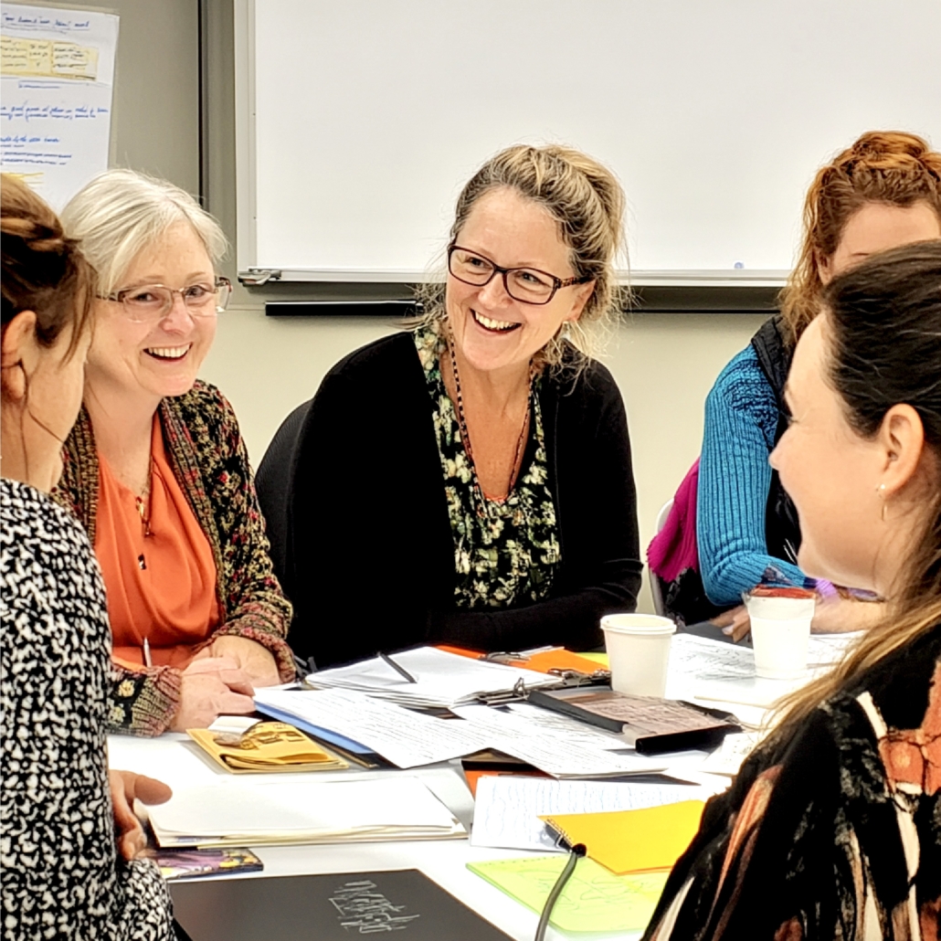 Groepssessie leren volgens de Leren Leren Methode Mensen in een groepssessie werken samen aan leermethodes, lachen en overleggen rond een tafel met documenten en kopjes.